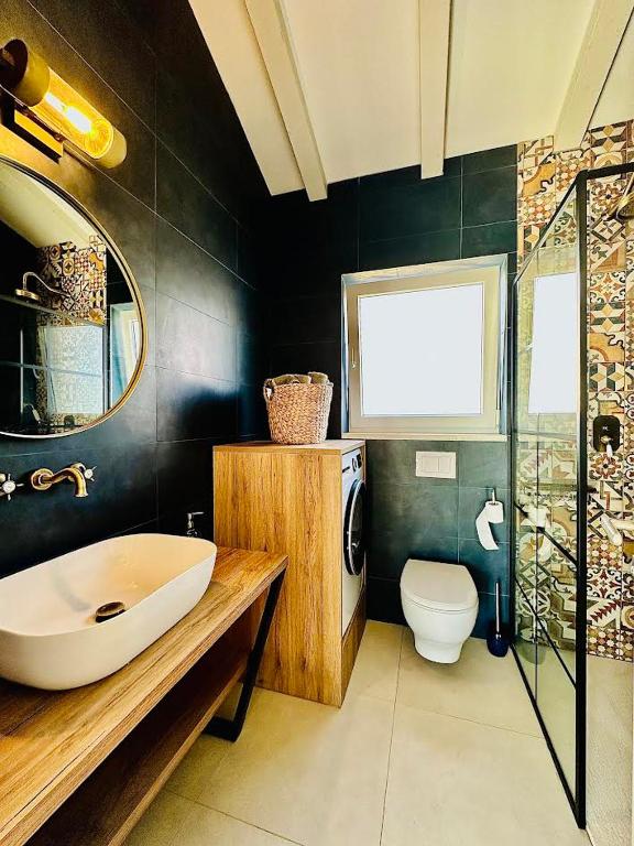 Dark-tiled bathroom with round mirror, wooden vanity and patterned shower in Lovers Nest